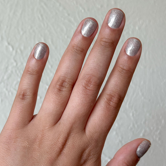 Hand with nails painted in Platinum Velvet - Gel showing sheer silver shimmer manicure with sparkling magnetic polish finish