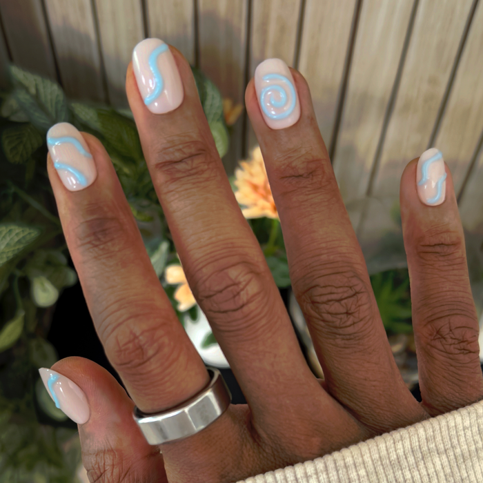 Puffy Swirls - Press-On | Short | Round neutral nails with raised blue swirl accents on hand against floral background