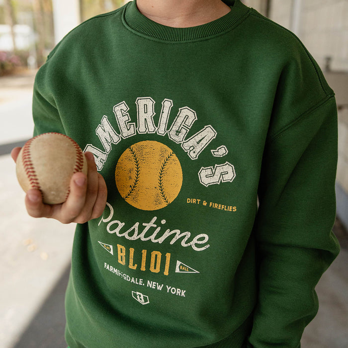 Close up of child wearing a forest green America's Pastime crewneck sweatshirt holding a baseball.