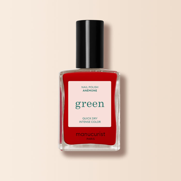 A bottle of Manucurist Anémone nail polish from the Green™ range, in a vibrant red shade, housed in a rectangular clear glass bottle with a black cap and a white label displaying product details.