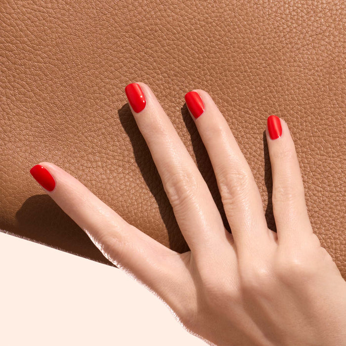 A hand with neatly manicured nails painted in Anémone by Manucurist rests on textured brown leather.