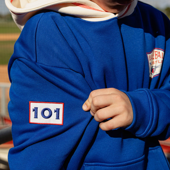 Close up of royal blue champions hoodie sleeve showing embroidered 101 patch and Baseball Lifestyle shield chest graphic