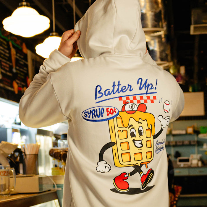 Person wearing a hoodie with a cartoon waffle character and 'Batter Up!' text in a casual setting