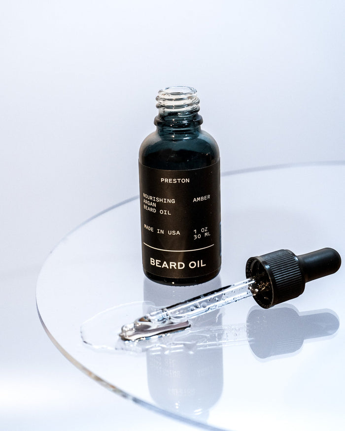 Amber beard oil bottle and dropper tip with a few drops on glass