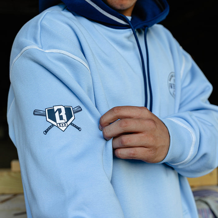Detail shot of the BL101 crossed bats home plate logo on the left sleeve of the columbia blue BL101 Bat Co Hoodie.