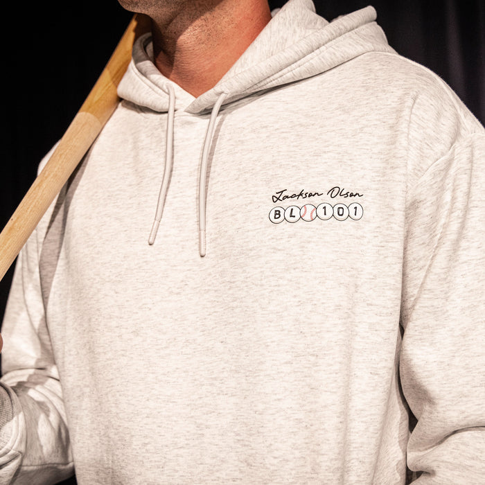 Close-up of the chest graphic on the heather gray BSBL Era hoodie, showing the "Jackson Olson" script above the BL101 baseball bead logo