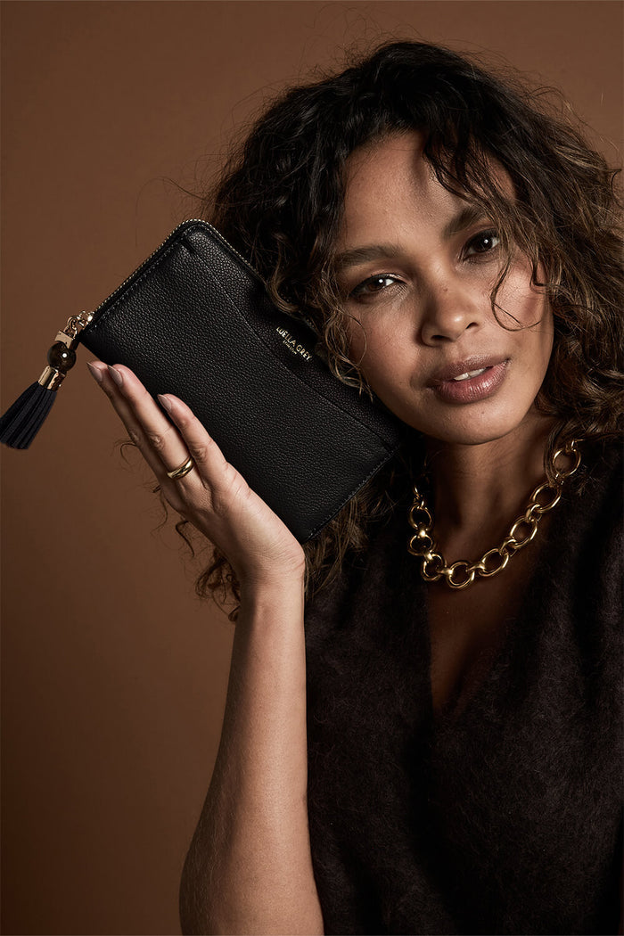 Female model holding Capriana Black faux leather Large Purse with one hand next to her face