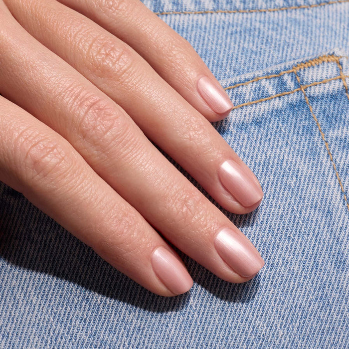 A hand with neatly manicured nails painted in Manucurist’s Carnation, a pearly pink beige polish, rests on blue denim fabric and catches the light with a subtle shimmer.