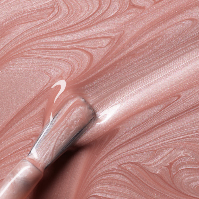 A close-up of a brush spreading Manucurist Carnation nail polish in pearly pink beige swirls with a shimmery finish.