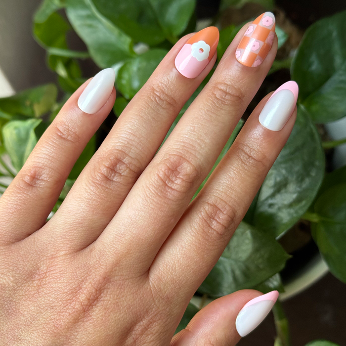 Chrome Flower Mixed Pack - Press-On | Medium | Almond with floral and checkered pastel designs on natural hand over green leaves background