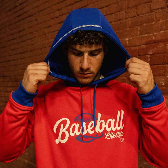Man pulling up the royal blue hood of a red Baseball Lifestyle hoodie against a brick wall