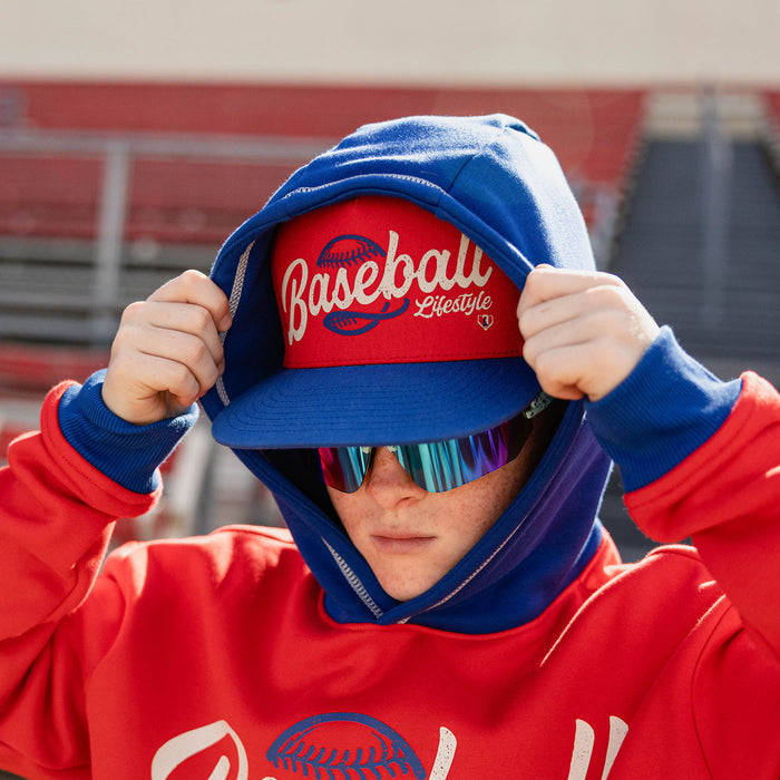 Boy pulling the royal blue hood over a red Baseball Lifestyle snapback wearing iridescent shield sunglasses and a red Baseball Lifestyle hoodie
