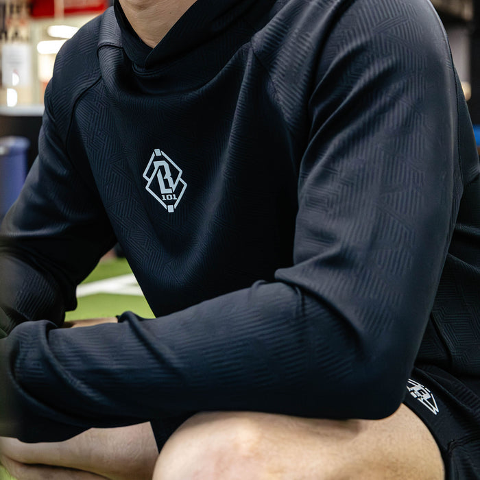 Person wearing a black athletic outfit with a logo on a blurred sports field background