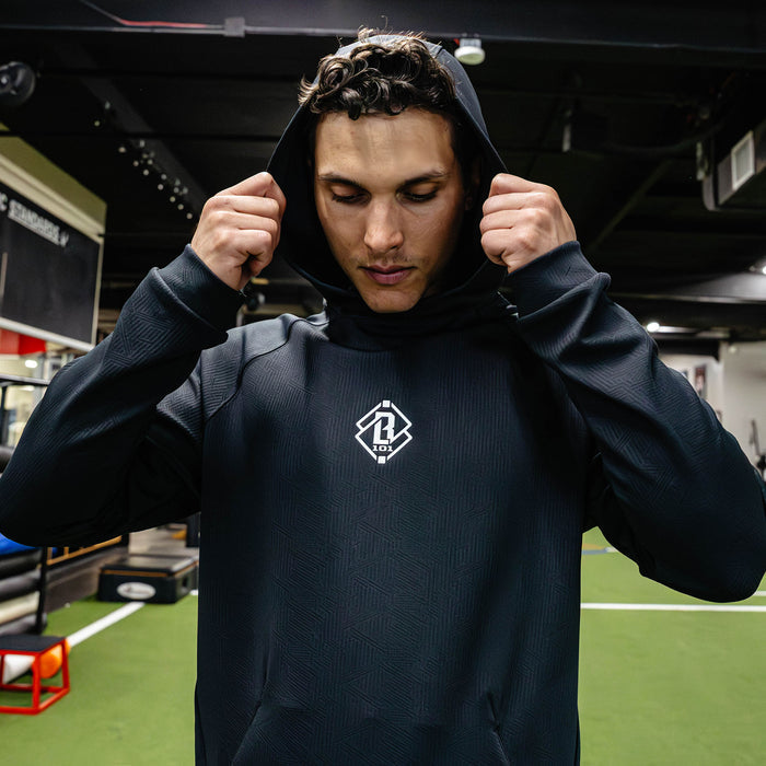 Person wearing a dark hoodie with a logo in an indoor sports facility