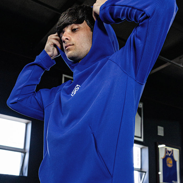 Person wearing a blue hoodie with a logo, standing indoors.