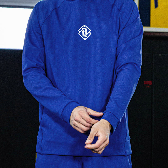 Person wearing a blue tracksuit with a logo on the chest against a dark background