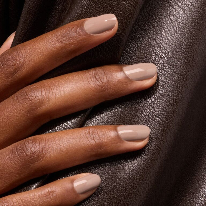A hand with neatly manicured nails painted in Dove Beige by Manucurist rests on textured dark brown leather fabric.