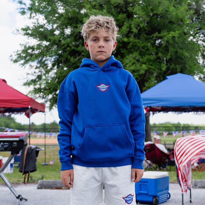 Fastball Flight Hoodie - Blue: Front-facing youth male model wearing royal blue Fastball Flight hoodie with heather gray Fastball Flight sweatshorts at outdoor baseball event
