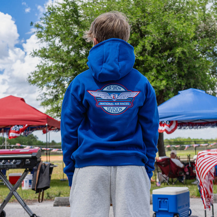 Back view of youth male model showing Air Show National Air Races Division badge on royal blue hoodie with heather gray sweatshorts at outdoor baseball event