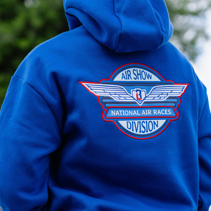 Close-up back detail of youth model showing Air Show National Air Races Division embroidered badge on royal blue hoodie outdoors