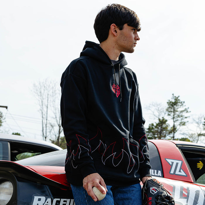Male model in side profile leaning against a race car outdoors wearing a black hoodie with BL101 flame crest on the chest and stitched flame detailing on the sleeves