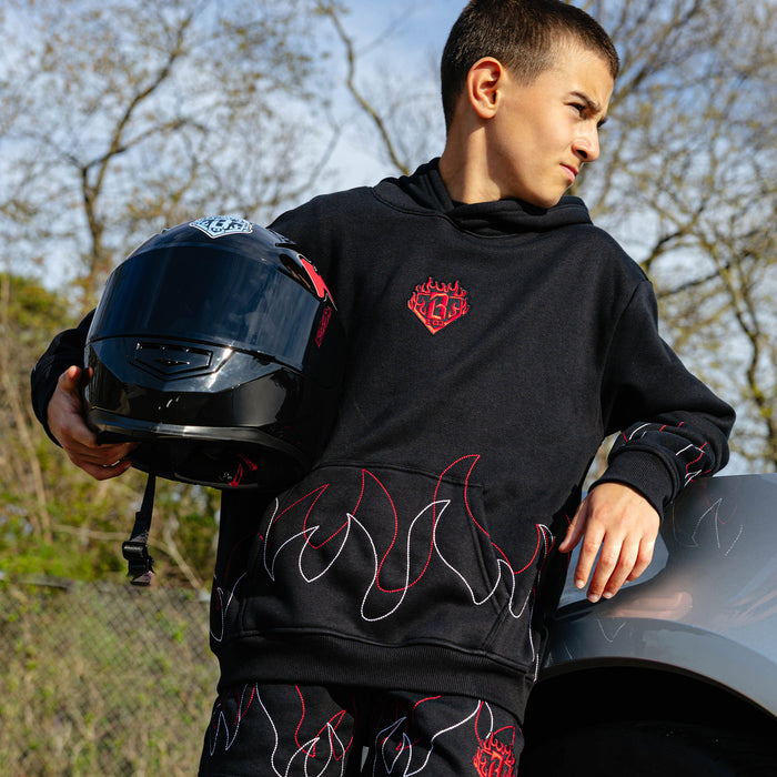 Young male model holding a racing helmet outdoors wearing a black hoodie with BL101 flame crest embroidery and stitched flame detailing along the hem and sleeves