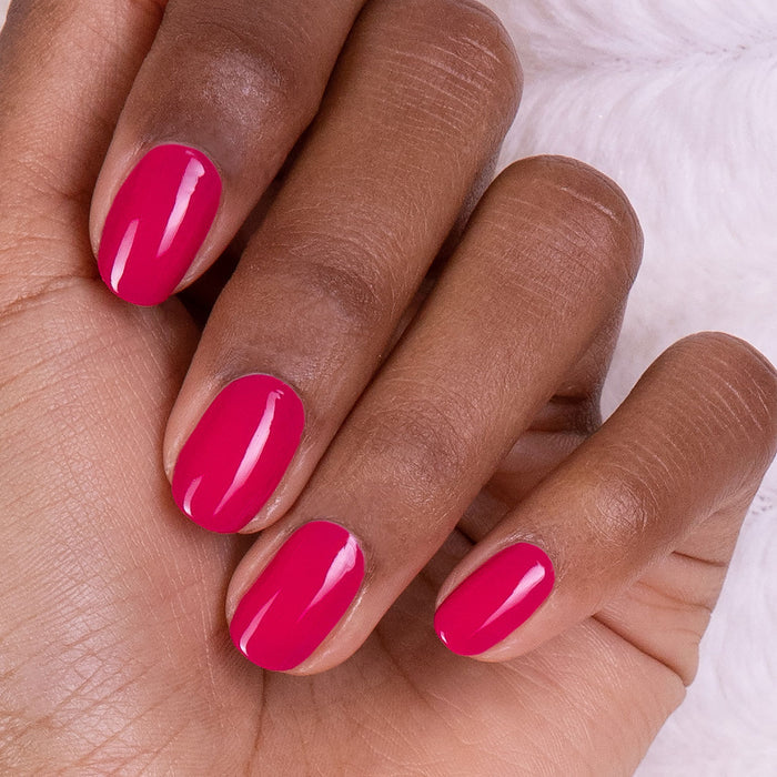 A close-up of a hand with neatly manicured nails painted in Manucurist's Fuchsia nail polish, resting on a soft white surface.