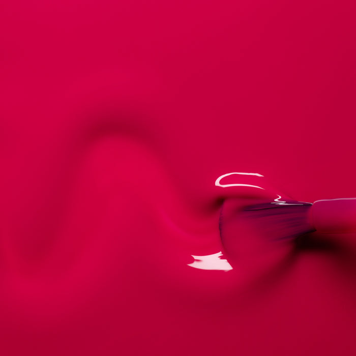 A close-up of a brush applies Manucurist's Fuchsia nail polish in a wavy line, revealing glossy reflections and a vibrant, bold look.