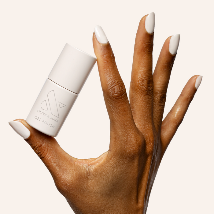 Hand with almond-shaped nails painted in soft white shade holding LHG - Gel polish bottle on neutral background