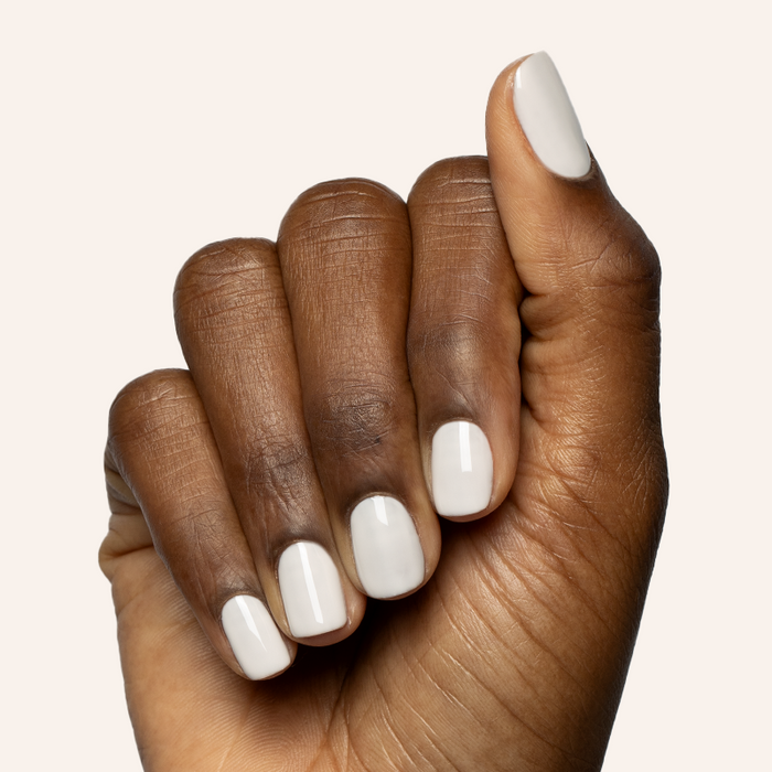 Hand with short rounded nails polished in soft off-white shade using LHG - Gel polish on plain light background