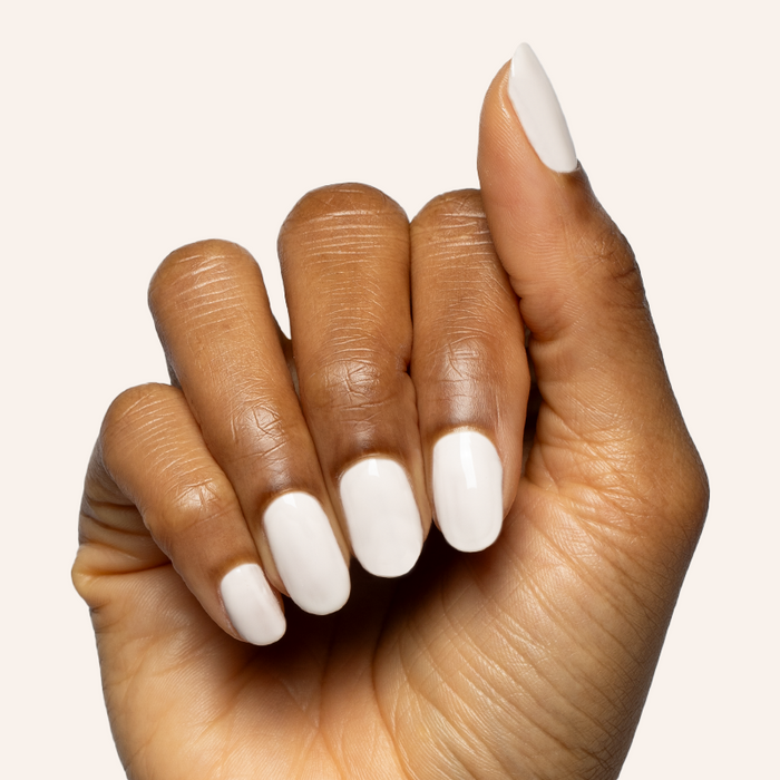 Hand with medium rounded nails painted in soft white shade using LHG - Gel polish on light background