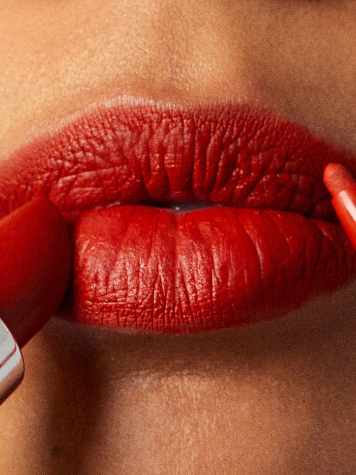 Dirty Love -- close up of model lips applying red lipstick and lip liner to top and bottom lip