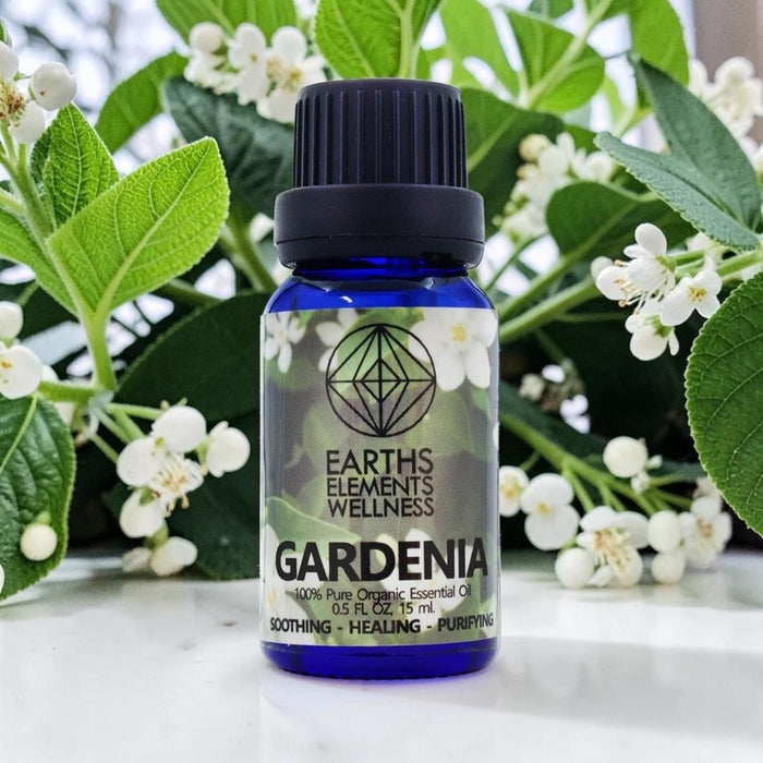 Bottle of Earths Elements Wellness Gardenia essential oil with gardenia flowers in the background
