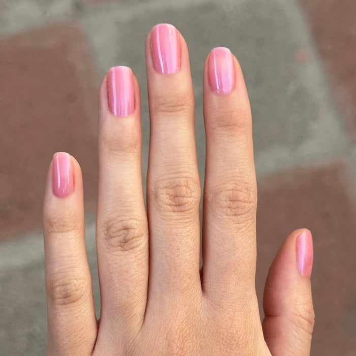 Hand with nails painted sheer bubble gum pink-blue iridescent using Olive Y’all - Gel polish for a fresh mani look