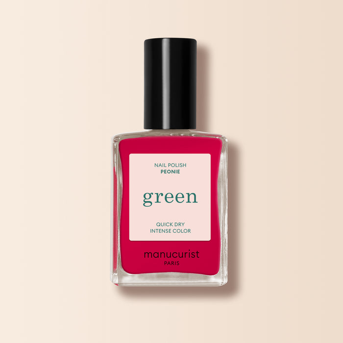 A bottle of Manucurist Péonie nail polish in a bright pink shade, featuring a black cap and a "green, quick dry intense color" label, is displayed against a cream background.