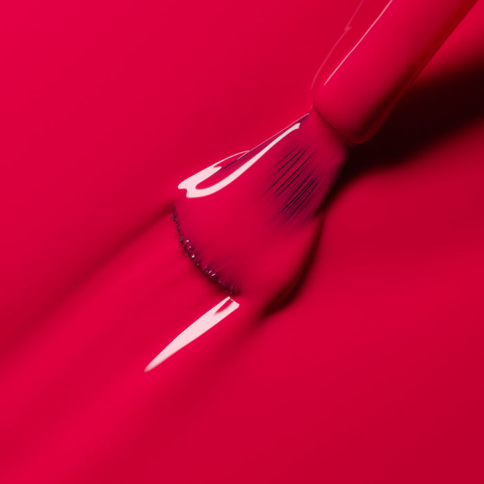 A close-up of a brush applying Péonie, a vibrant raspberry pink nail polish from Manucurist’s Green™ range, with smooth, glossy strokes covering the surface.