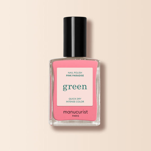 A bottle of Manucurist Pink Paradise nail polish from the Green range, featuring a black cap and pink label, sits on a light beige background.