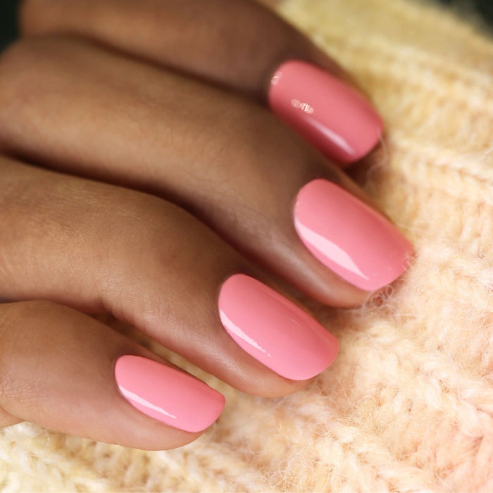 A close-up of neatly manicured nails painted in Manucurist’s Pink Paradise, a glossy candy pink polish, resting on cream-colored knit fabric.