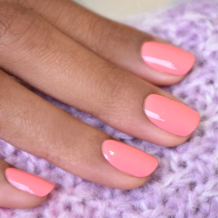 A close-up of a hand with neatly manicured nails painted in Manucurist's Pink Paradise polish, resting on soft lavender knit fabric.