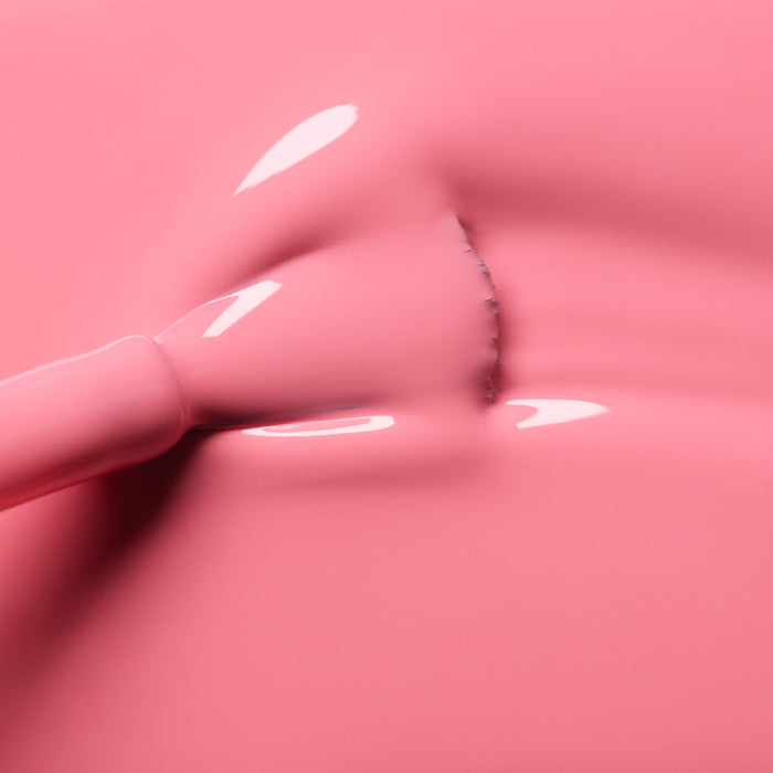 A close-up of a brush applying Manucurist's Pink Paradise from the Green range, spreading glossy candy pink polish in smooth, even strokes with reflective highlights.