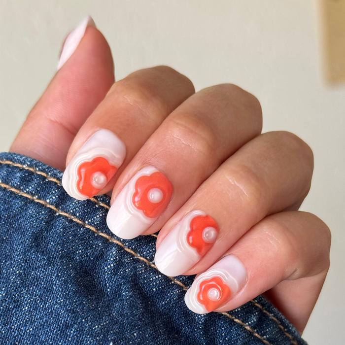 Puffy Bubble Flowers - Press-On | Short | Round neutral nails with raised orange flower designs on hand holding denim fabric