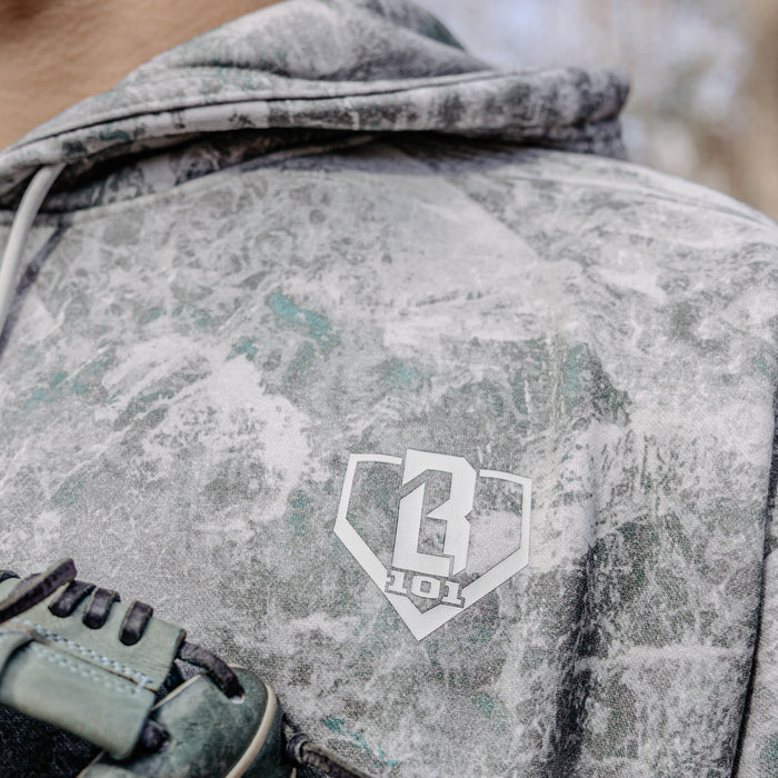 Close-up of a camouflage hoodie with a BL101 logo, featuring a glove in the foreground.