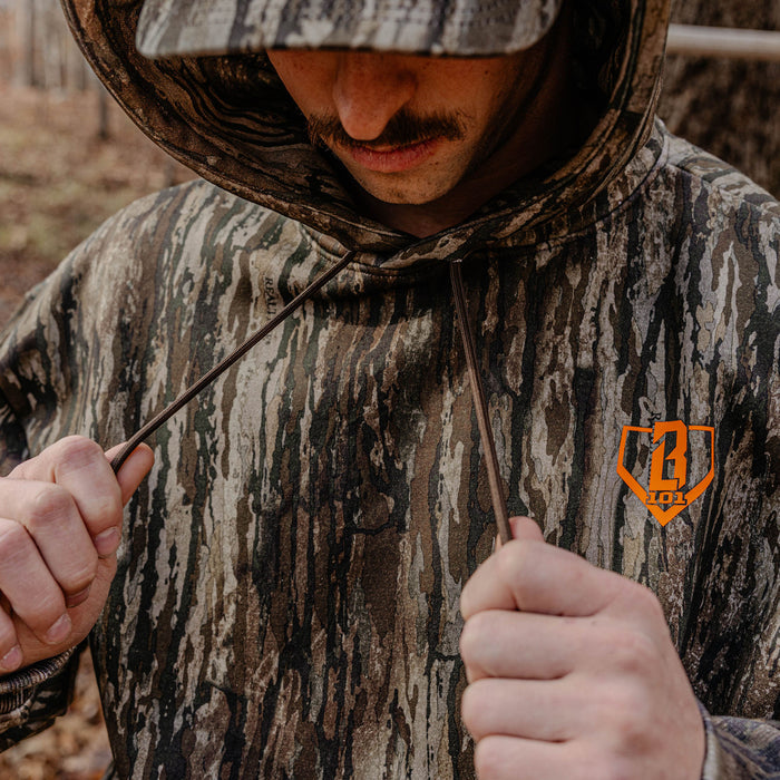 Person wearing a camouflage hoodie with orange BL101 logo, holding the strings.