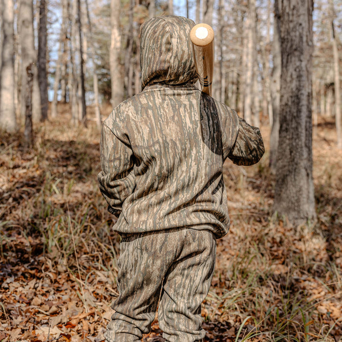 Person in camouflage hoodie and sweatpants holding a bat in a forest setting