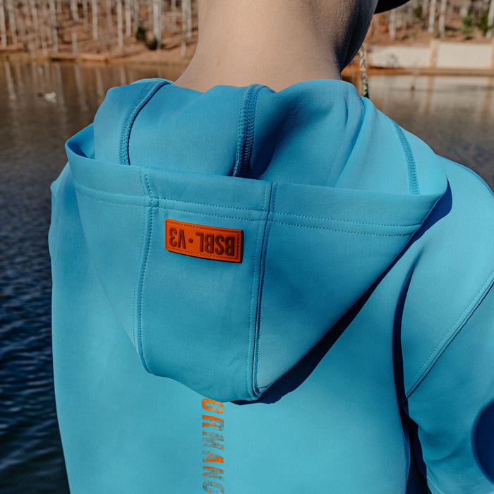 Person wearing a blue hoodie with a BSBL V3' logo, standing by a body of water.