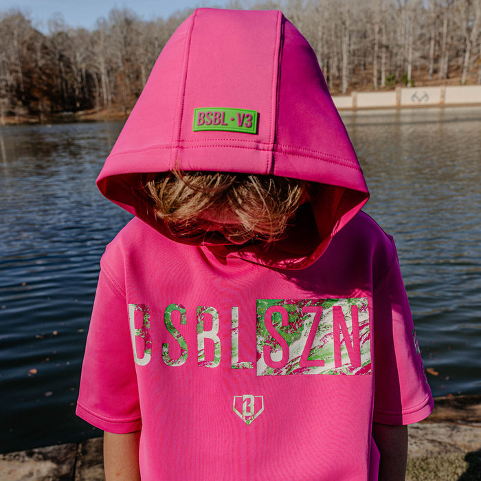 Person wearing a pink hoodie with 'BSBL V3' branding by a body of water.