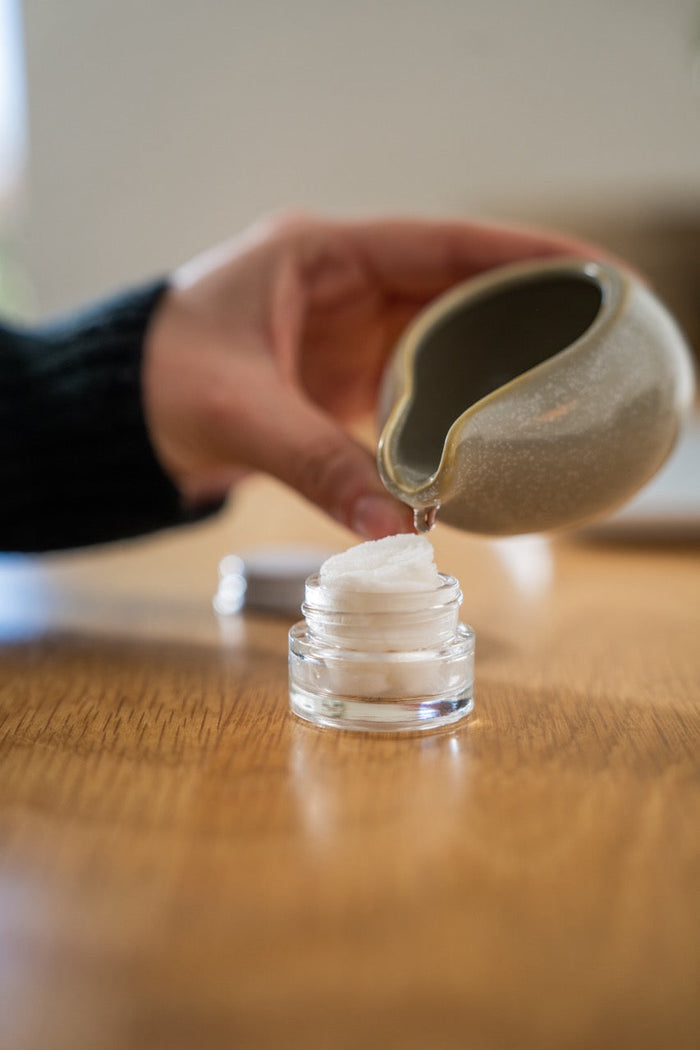 Aromatherapy eye cover set ingredient: hand pouring oil into small glass jar