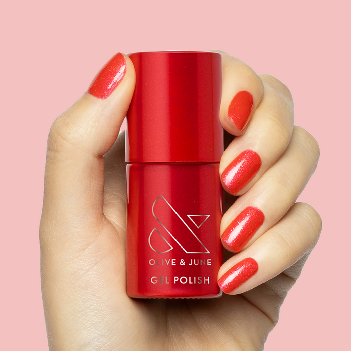 Hand holding bottle of Rodeo Queen - Gel with nails painted bright pinky-red shimmer gel polish on pink background