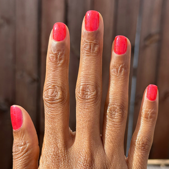 Hand with medium-length nails painted bright pinky-red shimmer using Rodeo Queen - Gel polish in natural light