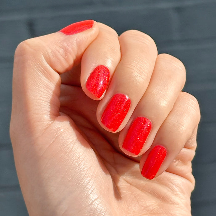 Hand with rounded nails painted bright pinky-red with silver shimmer using Rodeo Queen - Gel in natural light